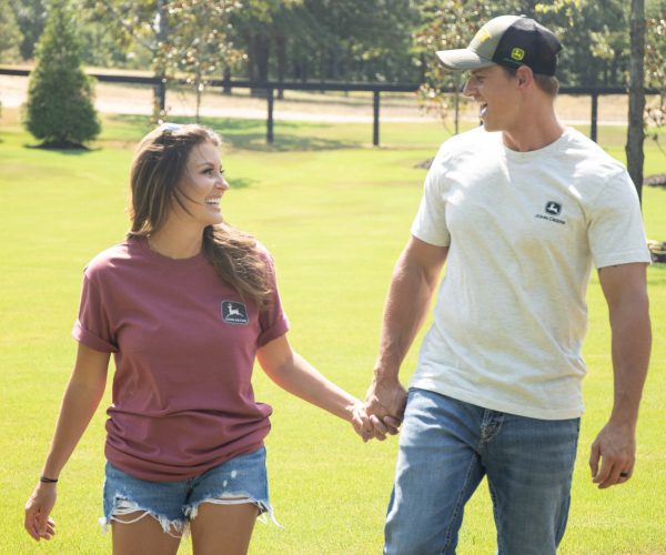 Image of a man wearing LP80134 the oatmeal colored John Deere unisex t shirt walking with a woman.