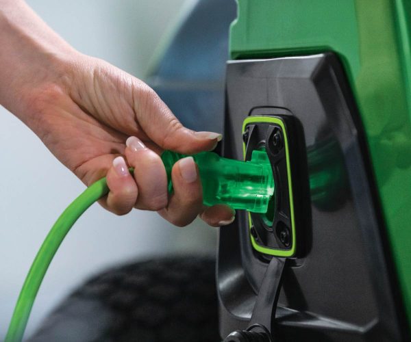 Image of a person plugging in the John Deere Z370R Electric ZTrak Zero Turn lawn mower to charge.