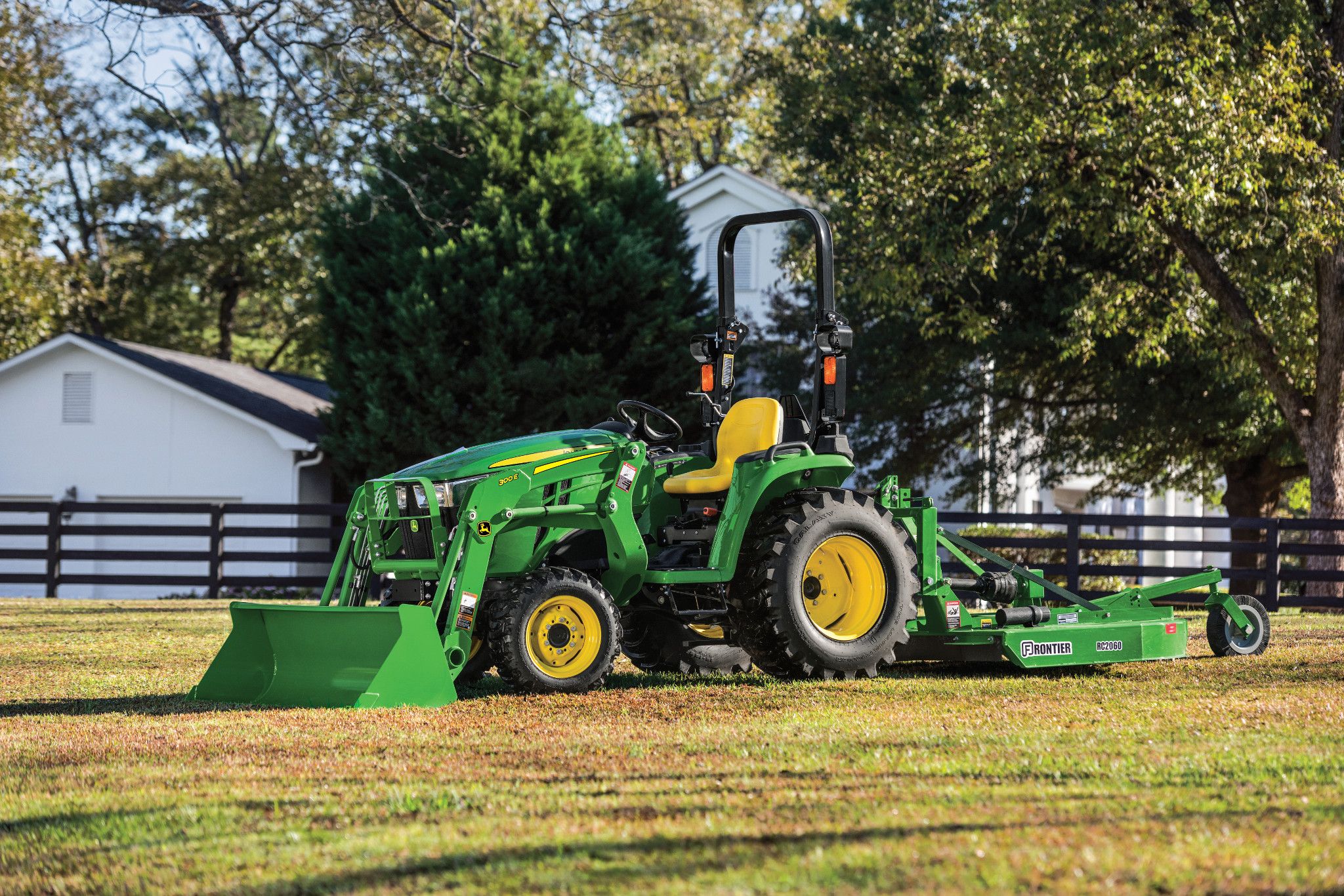 John Deere 3038E compact utility tractor with a 300E front loader and Frontier RC2060 rotary cutter parked on a rural property.